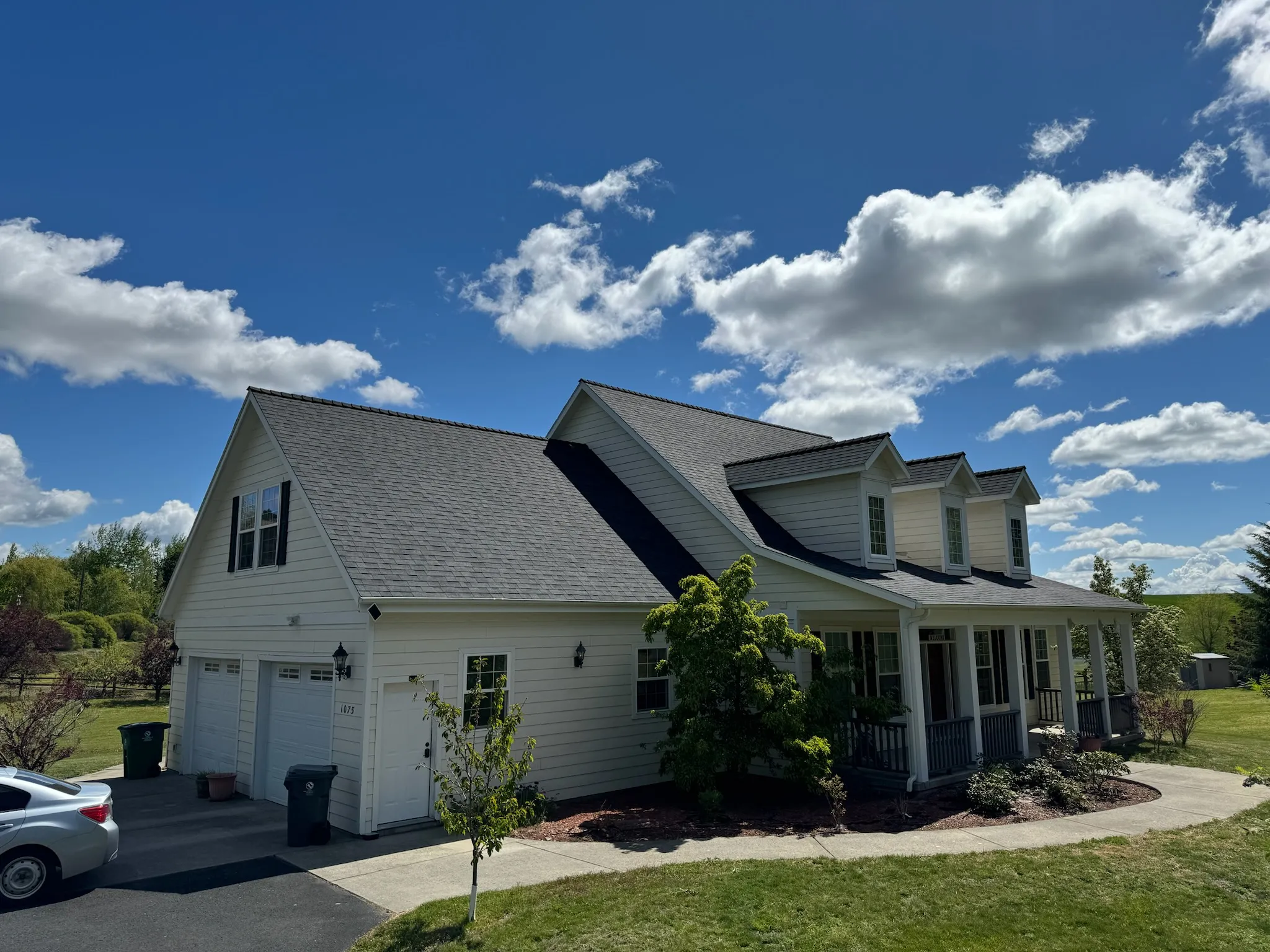 A finished architectural-shingle roof on a white two-story home under a blue Idaho sky
